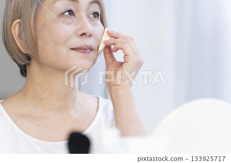 Senior woman putting on makeup by a bright window 133925717