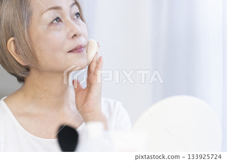 Senior woman putting on makeup by a bright window 133925724