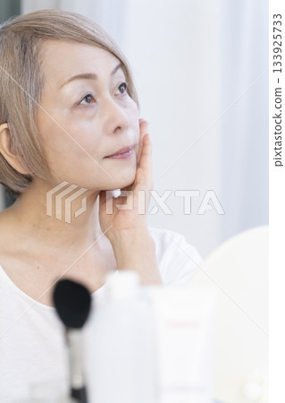Senior woman putting on makeup by a bright window Senior woman putting on makeup by a bright window 133925733