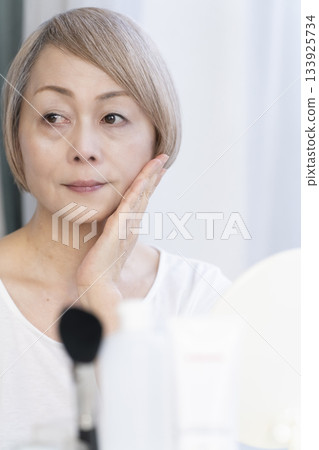 Senior woman putting on makeup by a bright window 133925734
