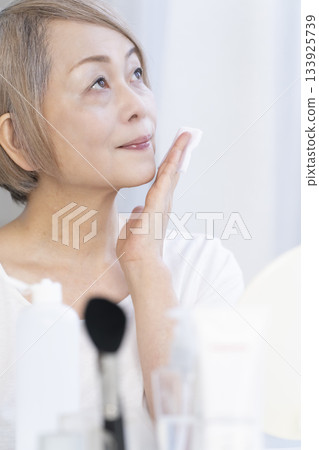 一位老婦人在明亮的窗邊化妝。 133925739