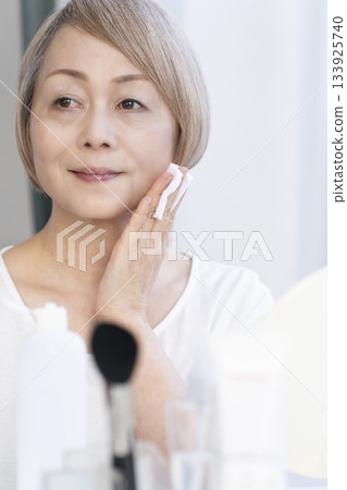Senior woman putting on makeup by a bright window 133925740
