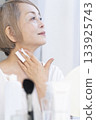 一位老婦人在明亮的窗邊化妝。 133925743