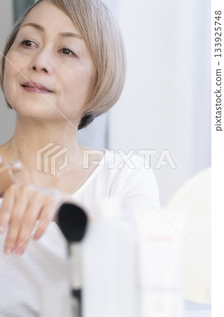 一位老婦人在明亮的窗邊化妝。 133925748