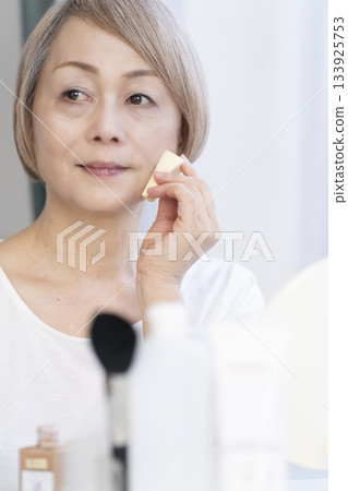 一位老婦人在明亮的窗邊化妝。 133925753