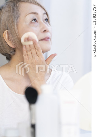 一位老婦人在明亮的窗邊化妝。 133925757