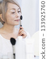 一位老婦人在明亮的窗邊化妝。 133925760