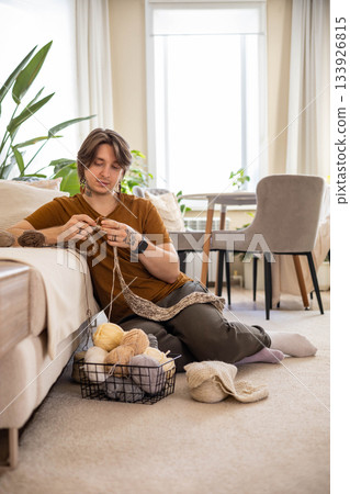 Feminine hipster man crochet handmade use hook knitting needles and wool yarn relaxing on couch Feminine hipster man crochet handmade use hook knitting needles and wool yarn relaxing on couch 133926815