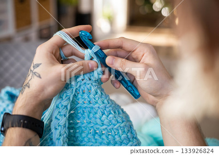 Man hands crochets handmade crocheting supplies assorted wool yarn hook knitting top view closeup Man hands crochets handmade crocheting supplies assorted wool yarn hook knitting top view closeup 133926824
