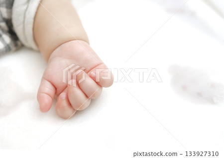 A close-up of a baby's tiny hand resting on a white futon. 133927310