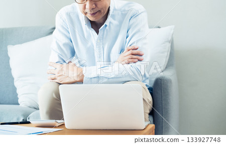A middle-aged man thinking while looking at a computer in the living room A middle-aged man thinking while looking at a computer in the living room 133927748
