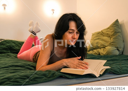 Russian 50 year old woman calmly turning a page while reading in bed enjoying a quiet mindful moment relaxation balance and gentle evening focus Russian 50 year old woman calmly turning a page while reading in bed enjoying a quiet mindful moment relaxation balance and gentle evening focus 133927814