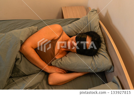 Sleeping 50 year old Russian woman rests on her side in a sleep mask, showing calmness, deep relaxation and a peaceful mindful night routine. Sleeping 50 year old Russian woman rests on her side in a sleep mask, showing calmness, deep relaxation and a peaceful mindful night routine. 133927815
