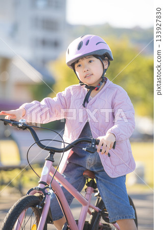 Bright park outdoor scene with Japanese girl riding a pink bicycle 133927830