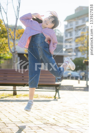 明亮的戶外景色,一位小學生在公園裡活力四射地跳躍。 明亮的戶外景色,一位小學生在公園裡活力四射地跳躍。 133927838