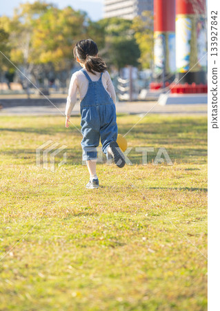 公園裡，一個幼稚園小女孩背對著鏡頭，在草地上追著球跑。 133927842