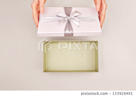 Woman opening empty gift box silver ribbon bow Cloud Dancer background Woman opening empty gift box silver ribbon bow Cloud Dancer background 133928491