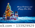Snowmen wearing colorful hat and scarf standing on snowy floor with gift box and illuminated Christmas tree in the night. 133929929