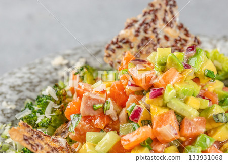 Fresh salmon and avocado tartare with diced vegetables and crispy seed chips served as a colorful gourmet appetizer 133931068