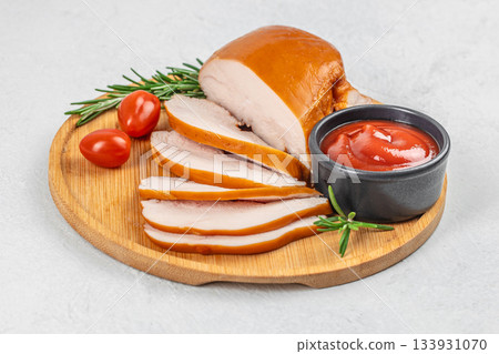 Sliced smoked chicken breast served on a wooden board with cherry tomatoes, rosemary, and ketchup on a light background 133931070