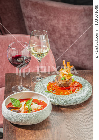 Elegant fine dining table setting with surf and turf steak, seafood soup and glasses of red and white wine in a modern restaurant Elegant fine dining table setting with surf and turf steak, seafood soup and glasses of red and white wine in a modern restaurant 133931089
