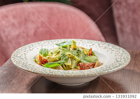 Pappardelle pasta with creamy basil pesto, chicken pieces, sun-dried tomatoes and pine nuts served in a decorative bowl Pappardelle pasta with creamy basil pesto, chicken pieces, sun-dried tomatoes and pine nuts served in a decorative bowl 133931092