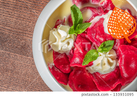 Bright red dumplings served with sweet cream sauce, fresh mint leaves and decorative garnish for a vibrant dessert presentation Bright red dumplings served with sweet cream sauce, fresh mint leaves and decorative garnish for a vibrant dessert presentation 133931095