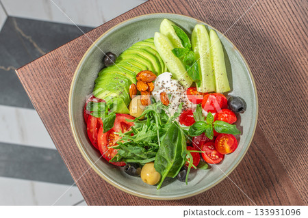 Fresh vibrant salad bowl with avocado, cucumbers, tomatoes, greens, olives, nuts and creamy cheese for a healthy colorful meal presentation Fresh vibrant salad bowl with avocado, cucumbers, tomatoes, greens, olives, nuts and creamy cheese for a healthy colorful meal presentation 133931096