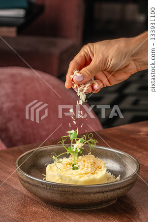 Hand sprinkling freshly grated parmesan over a gourmet plated dish with creamy puree and microgreens in a fine dining restaurant Hand sprinkling freshly grated parmesan over a gourmet plated dish with creamy puree and microgreens in a fine dining restaurant 133931100