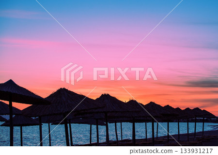 Seascape in the evening. Deserted tropical beach scenery with the silhouette of sun parasols and evening sky Seascape in the evening. Deserted tropical beach scenery with the silhouette of sun parasols and evening sky 133931217