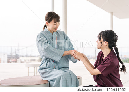 A female nurse talking to a female patient on the rooftop terrace of a hospital 133931662