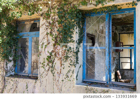 Abandoned Building With Blue Window Frames, Ivy Overgrowth And Broken Glassed Interiors Abandoned Building With Blue Window Frames, Ivy Overgrowth And Broken Glassed Interiors 133931669
