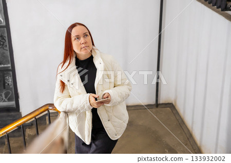 A Caucasian woman thoughtfully walks up the stairs with a phone in her hands. no makeup look or natural beauty. doctor, mother of two children, professor, businesswoman with long red hair A Caucasian woman thoughtfully walks up the stairs with a phone in her hands. no makeup look or natural beauty. doctor, mother of two children, professor, businesswoman with long red hair 133932002