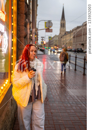 A happy woman drinks coffee in the evening on a neon lit street. date with lover A happy woman drinks coffee in the evening on a neon lit street. date with lover 133932003