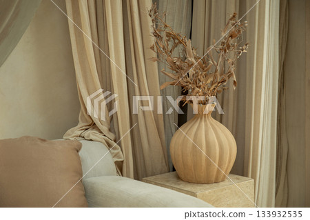 A stylish wooden vase holds dried flowers next to soft curtains 133932535