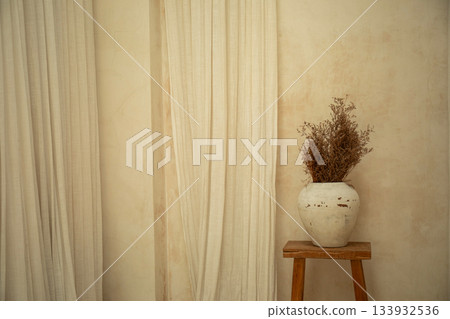 A cozy corner features a vase filled with dried flowers on a stool 133932536