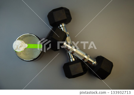 Black weights and a protein shake with a green spoon are arranged on a gray background, symbolizing fitness, strength training, and healthy nutrition choices Black weights and a protein shake with a green spoon are arranged on a gray background, symbolizing fitness, strength training, and healthy nutrition choices 133932713