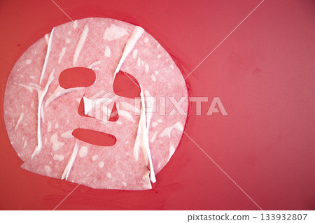 Soft facial mask on bright red background, highlighting skincare routine and beauty treatment, emphasizing relaxation and self-care in a visually appealing manner 133932807