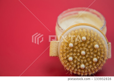Body scrub in a glass jar features a textured brush lid, placed on a vibrant red background, emphasizing beauty and self-care for skincare enthusiasts 133932816