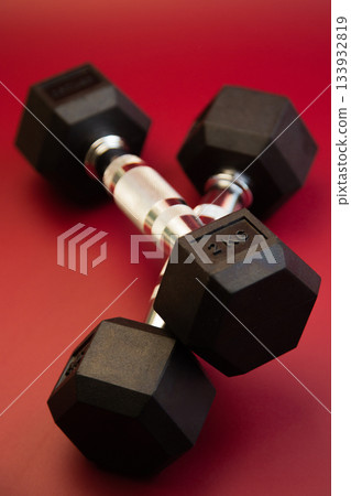 Hexagonal dumbbells with silver accents are positioned on a striking red surface, highlighting fitness gear ideal for strength training and enhancing workout sessions 133932819