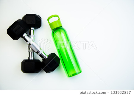 Dumbbells and a green water bottle are arranged on a white background, representing fitness and hydration, ideal for promoting health and wellness activities Dumbbells and a green water bottle are arranged on a white background, representing fitness and hydration, ideal for promoting health and wellness activities 133932857