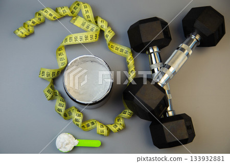 Fitness gear featuring dumbbells, measuring tape, and protein powder container on a gray background, illustrating healthy lifestyle and workout essentials Fitness gear featuring dumbbells, measuring tape, and protein powder container on a gray background, illustrating healthy lifestyle and workout essentials 133932881