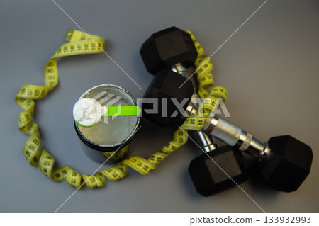 Black weights next to a protein powder container with a green scoop, surrounded by a measuring tape, illustrating fitness goals and healthy living choices Black weights next to a protein powder container with a green scoop, surrounded by a measuring tape, illustrating fitness goals and healthy living choices 133932993