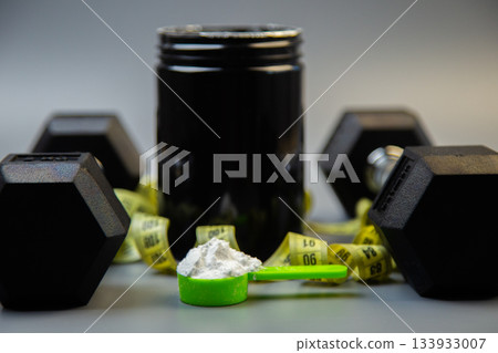 Fitness supplement container with green scoop filled with powder, surrounded by dumbbells, showcasing workout essentials and nutrition for health-conscious individuals Fitness supplement container with green scoop filled with powder, surrounded by dumbbells, showcasing workout essentials and nutrition for health-conscious individuals 133933007