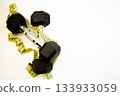 Dumbbells placed on a clean white background, intertwined with a yellow measuring tape, representing fitness, health, and the journey towards personal training success 133933059