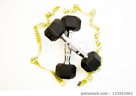 Dumbbells positioned on a clean white surface, surrounded by a measuring tape, representing fitness goals, health awareness, and the importance of physical activity for well-being Dumbbells positioned on a clean white surface, surrounded by a measuring tape, representing fitness goals, health awareness, and the importance of physical activity for well-being 133933061
