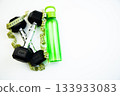 Fitness gear featuring black dumbbells, a vibrant green water bottle, and a measuring tape on a bright white background, representing a healthy lifestyle and exercise motivation 133933083