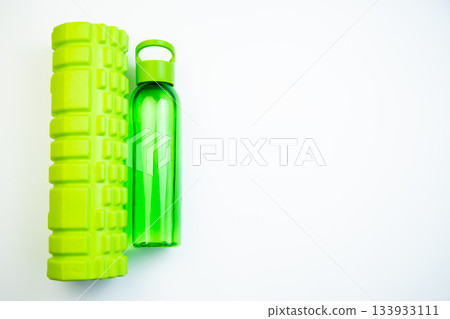 Green fitness foam roller and water bottle placed on a bright white surface, emphasizing wellness and exercise, perfect for active individuals and fitness routines 133933111