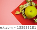 A yellow apple is artistically placed with a measuring tape on a colorful geometric background, representing themes of health, wellness, and nutrition in a creative setting 133933181