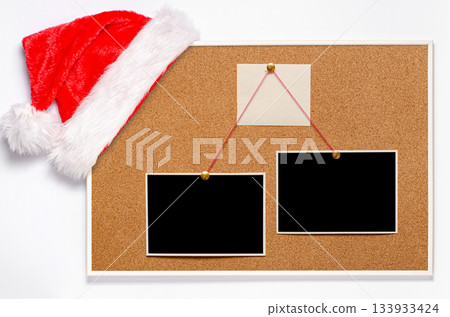 Blank paper notes and an empty photo are pinned to a cork board. Santa's hat on a cork board Blank paper notes and an empty photo are pinned to a cork board. Santa's hat on a cork board 133933424